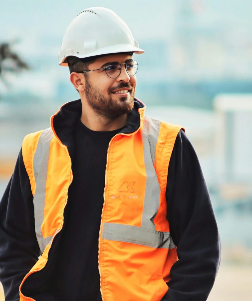 Construction worker wearing an orange reflective safety vest and white hard hat at a worksite